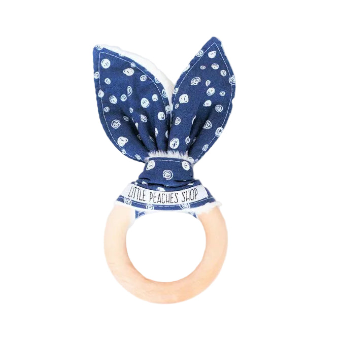 A navy-colored baby teether with a blue polka dot pattern and a wooden ring attached with organic beeswax.